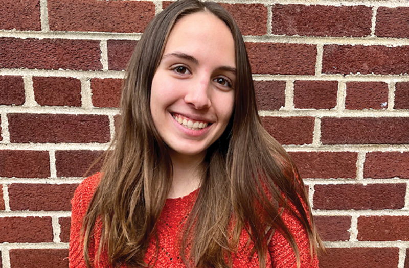 A young woman standing in front of a brick wall.